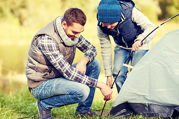 Image showing happy father and son setting up tent outdoors