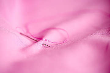 Image showing sewing needle with thread stuck into pink fabric