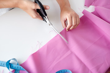 Image showing woman with tailor scissors cutting out fabric