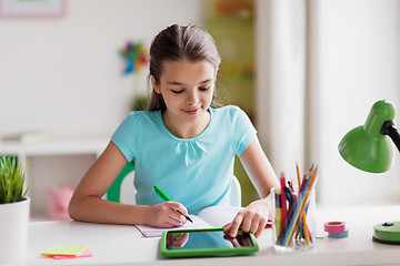 Image showing girl with tablet pc writing to notebook at home