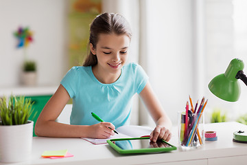 Image showing girl with tablet pc writing to notebook at home