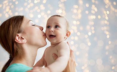 Image showing happy young mother kissing little baby over lights