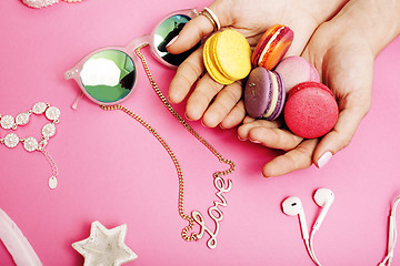 Image showing woman hands holding macaroons with lot of girl stuff on pink background, girls accessories concept