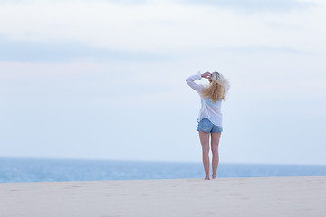 Image showing Woman on sandy beach in white shirt at dusk. 