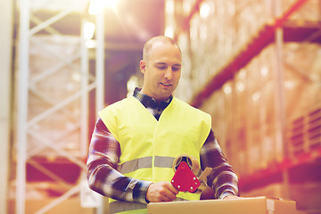 Image showing man in safety vest packing box at warehouse