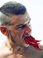 Image showing desperate young man with a lot of chilli pepper in mouth, lookin