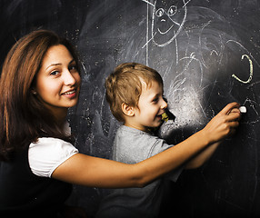 Image showing little cute boy with young teacher in classroom studying at blackboard smiling, doing homework