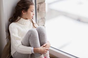 Image showing sad girl sitting on sill at home window in winter