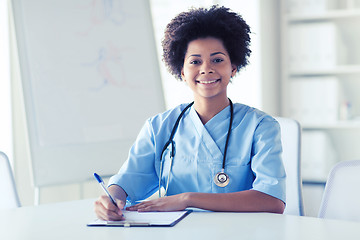 Image showing happy female doctor or nurse writing to clipboard