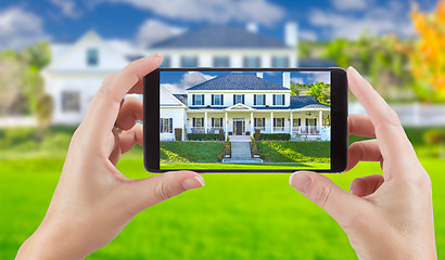 Image showing Female Hands Holding Smart Phone Displaying Photo of House Behin