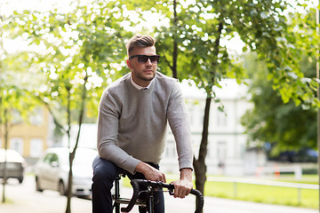 Image showing young man in shades riding bicycle on city street