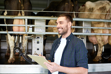 Image showing man with clipboard and milking cows on dairy farm