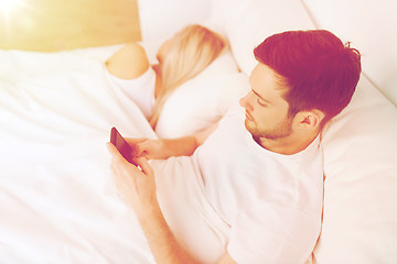 Image showing man texting message while woman is sleeping in bed
