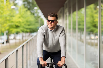 Image showing young man in shades riding bicycle on city street