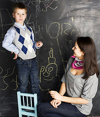 Image showing little cute boy with young teacher in classroom studying at blackboard smiling, doing homework