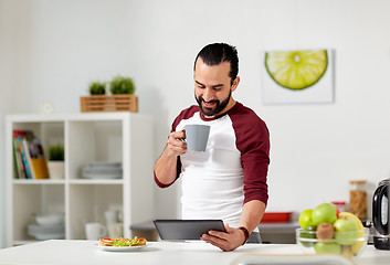 Image showing man with tablet pc eating at home kitchen