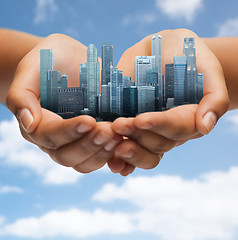 Image showing hands holding city over blue sky background