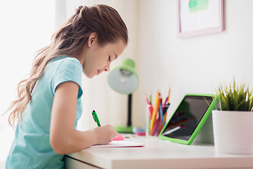 Image showing girl with tablet pc writing to notebook at home