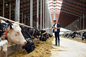 Image showing farmer with clipboard and cows in cowshed on farm