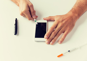 Image showing close up of man with smartphone making blood test