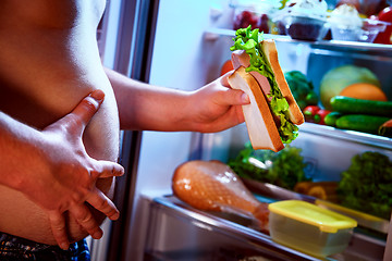 Image showing Hungry man holding a sandwich in his hands and standing next to 