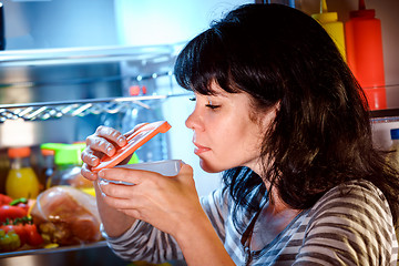 Image showing Woman opened the refrigerator and sniffs a container of food