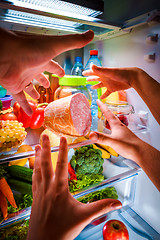 Image showing Human hands reaching for food at night in the open refrigerator