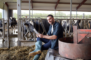 Image showing young man with tablet pc and cows on dairy farm