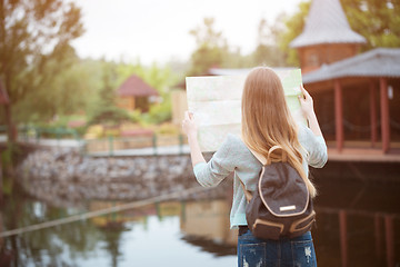 Image showing Back side of traveler girl searching right direction on map, orange sunset light, traveling along Europe