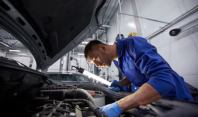 Image showing mechanic man with lamp repairing car at workshop