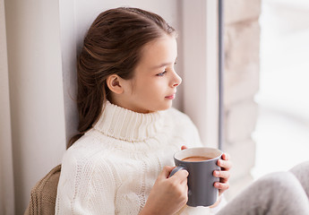 Image showing girl with cacao mug sitting at home window
