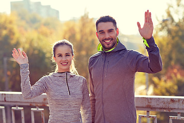 Image showing smiling couple waving hand outdoors