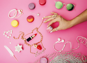 Image showing woman hands holding macaroons with lot of girl stuff on pink background, girls accessories concept 