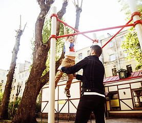 Image showing little cute blond boy hanging on playground outside, father training with fun, lifestyle children concept