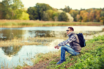 Image showing man with backpack resting on river bank