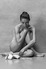 Image showing Tired ballet dancer sitting on the wooden floor on a pink background