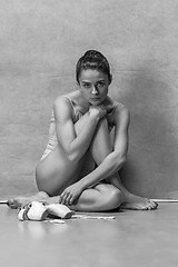 Image showing Tired ballet dancer sitting on the wooden floor on a pink background