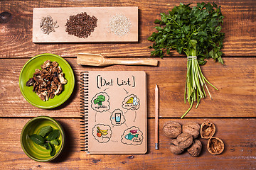 Image showing Notebook for recipes, walnuts, parsley and seeds on wooden table.