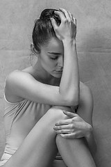 Image showing Tired ballet dancer sitting on the wooden floor on a pink background