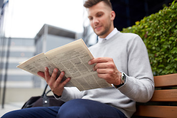 Image showing man reading newspaper on city street bench
