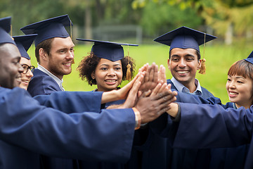 Image showing happy students in mortar boards making high five