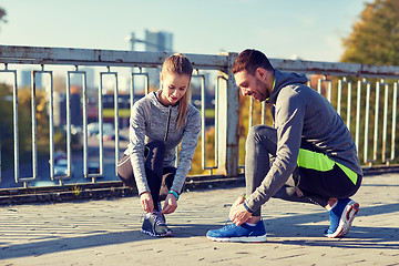 Image showing smiling couple tying shoelaces outdoors