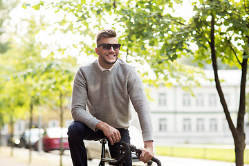 Image showing young man in shades riding bicycle on city street