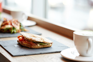 Image showing salmon panini sandwich on stone plate at cafe