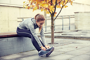 Image showing happy young sporty woman tying shoelaces outdoors