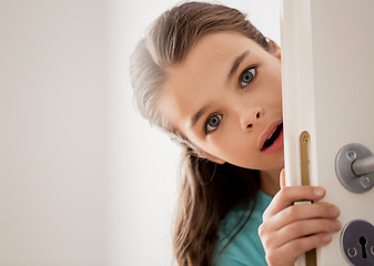 Image showing scared beautiful girl hiding behind door at home