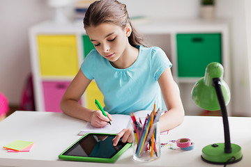 Image showing girl with tablet pc writing to notebook at home