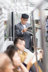 Image showing Japanese businessman taking ride to work in morning, standing inside public transport and reading newspaper.