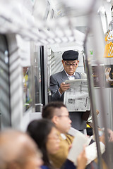 Image showing Japanese businessman taking ride to work in morning, standing inside public transport and reading newspaper.