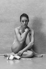 Image showing Tired ballet dancer sitting on the wooden floor on a pink background